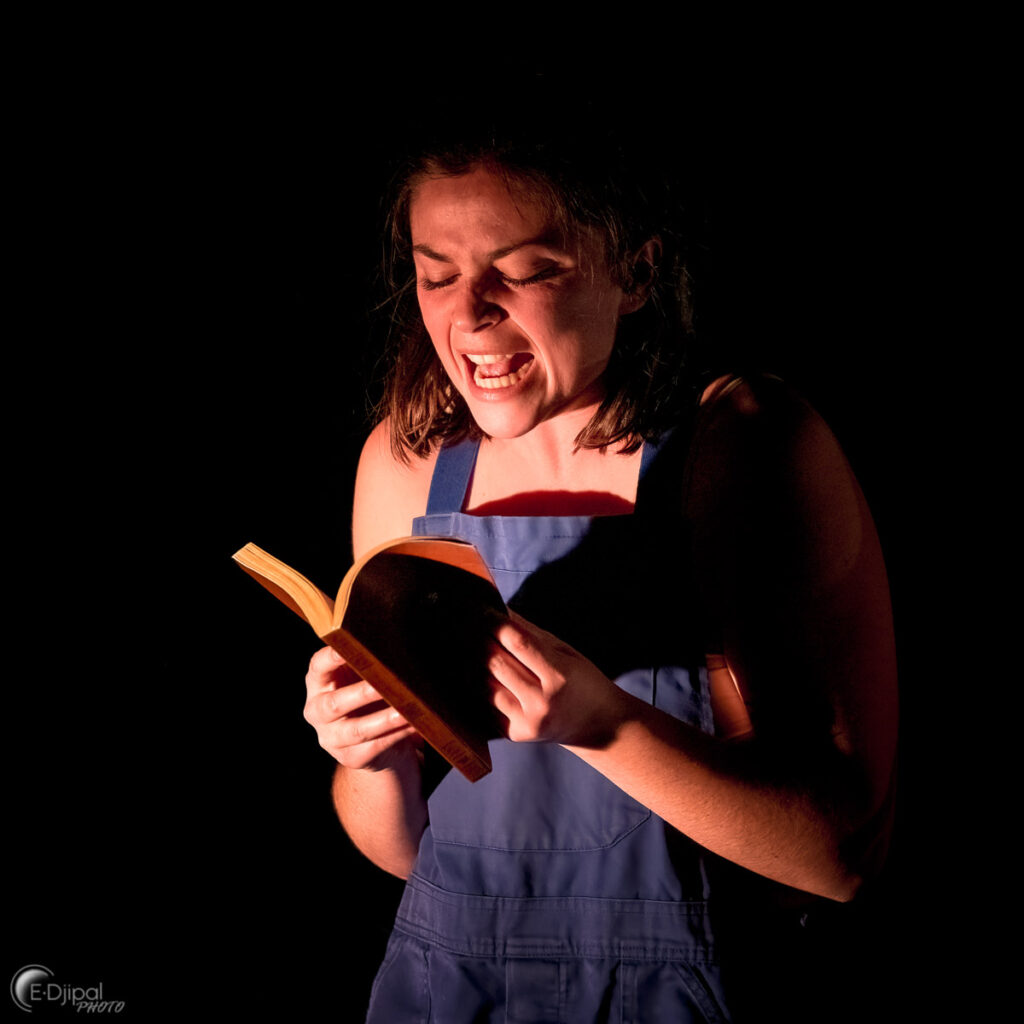 Julie Deniel en train de lire un livre avec une expression intense sur le visage, sur fond noir.